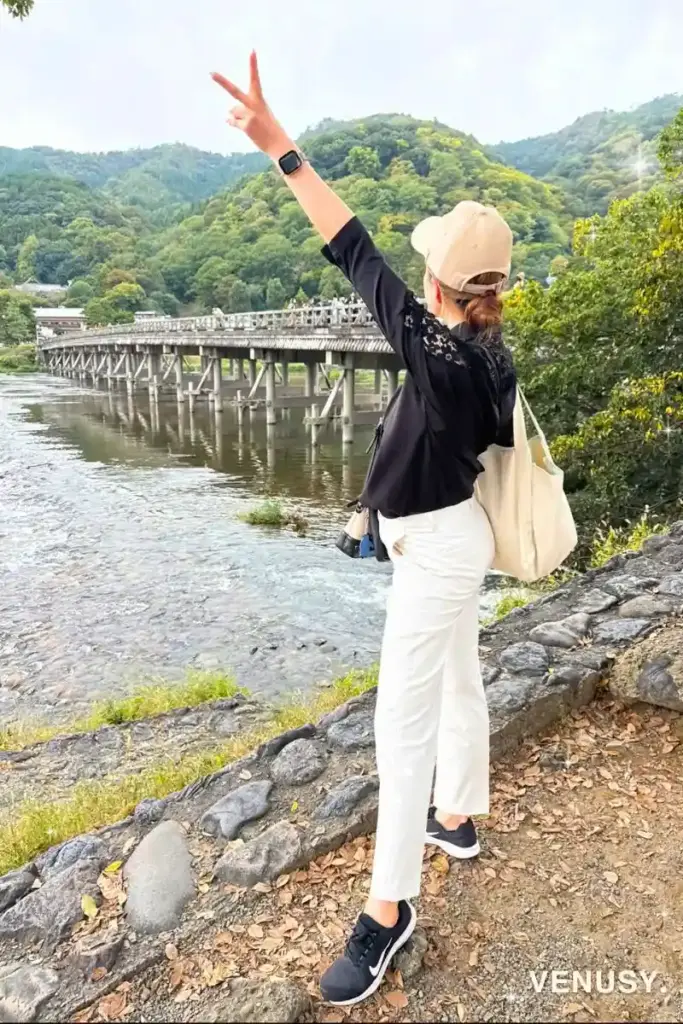 スタバ福袋のトートバッグを肩にかけて嵐山・渡月橋でピースする女性の後ろ姿