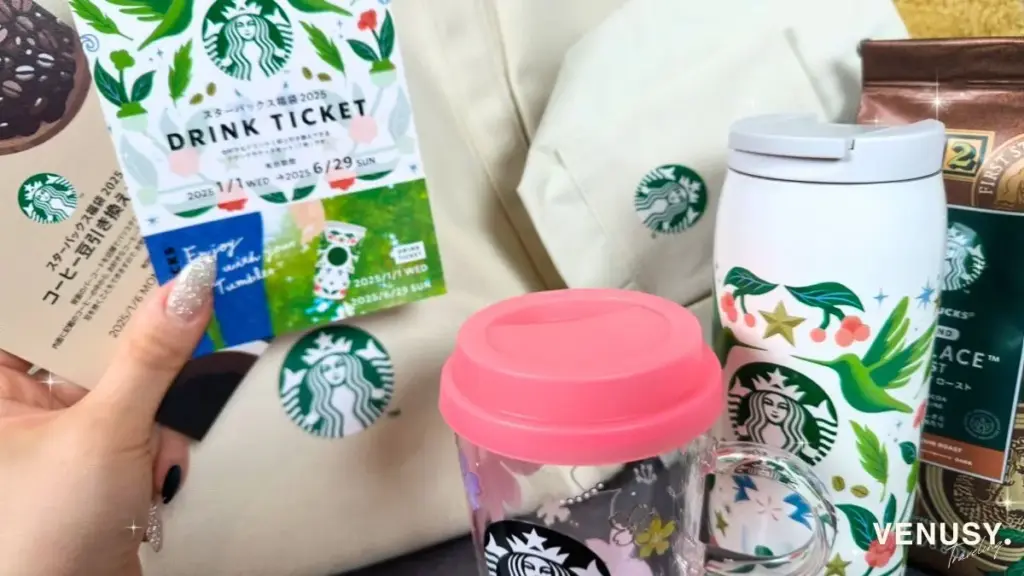 スタバ福袋2025の中身すべてを紹介した写真。ドリンクチケット、ピンクの蓋付きカップ、白いタンブラー、コーヒー豆、白いトートバッグが並べられている。